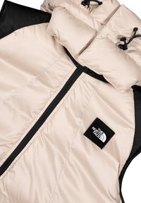 Gilet imbottito in beige chiaro con dettagli neri, caratterizzato da un alto colletto, chiusura con zip e applicazione del logo sul petto. Tessuto liscio e isolato.