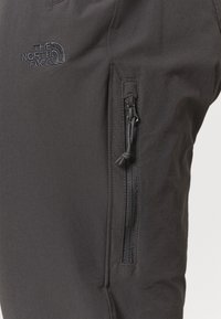 Zwarte outdoor broek met een geborduurd logo, een zijzak met rits en een togglesluiting, en een gladde, matte stoftextuur.