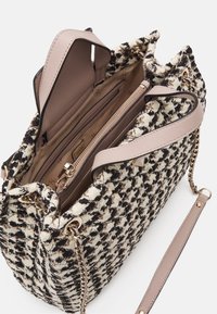 Sac à main en tweed noir et crème avec une forme structurée, doté d'une bandoulière en cuir rose clair et d'une quincaillerie dorée. Compartiments intérieurs visibles.