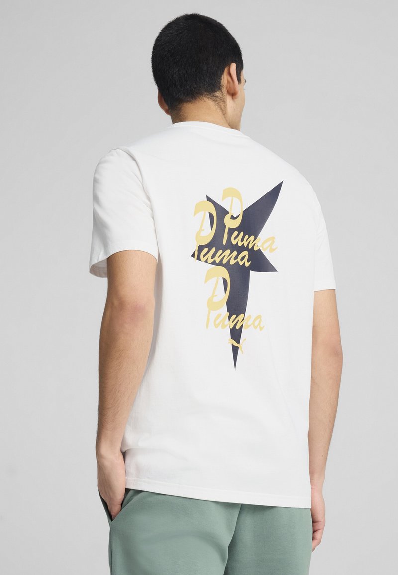 Hvid kortærmet t-shirt med et stort grafisk motiv på ryggen i mørkeblåt og gyldent tekst, der viser brandnavne i en stjernesystem-agtig form.