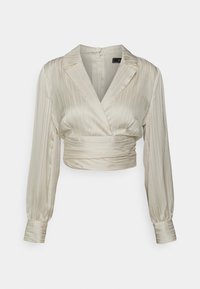 Blouse raccourcie en satin beige clair avec plis verticaux, col châle, manches longues et ourlets retroussés, présentant un design enveloppant autour de la taille.