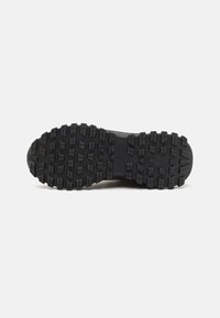 Black rubber shoe sole featuring deep treads and traction patterns. Textured surface for grip, with a rounded toe and reinforced heel area.
