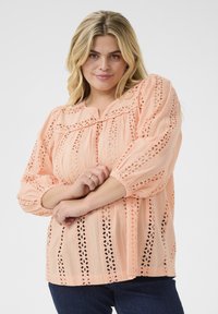 Light peach blouse with lace detailing, round neckline, and long, puffed sleeves. Features eyelet patterns and a relaxed fit.