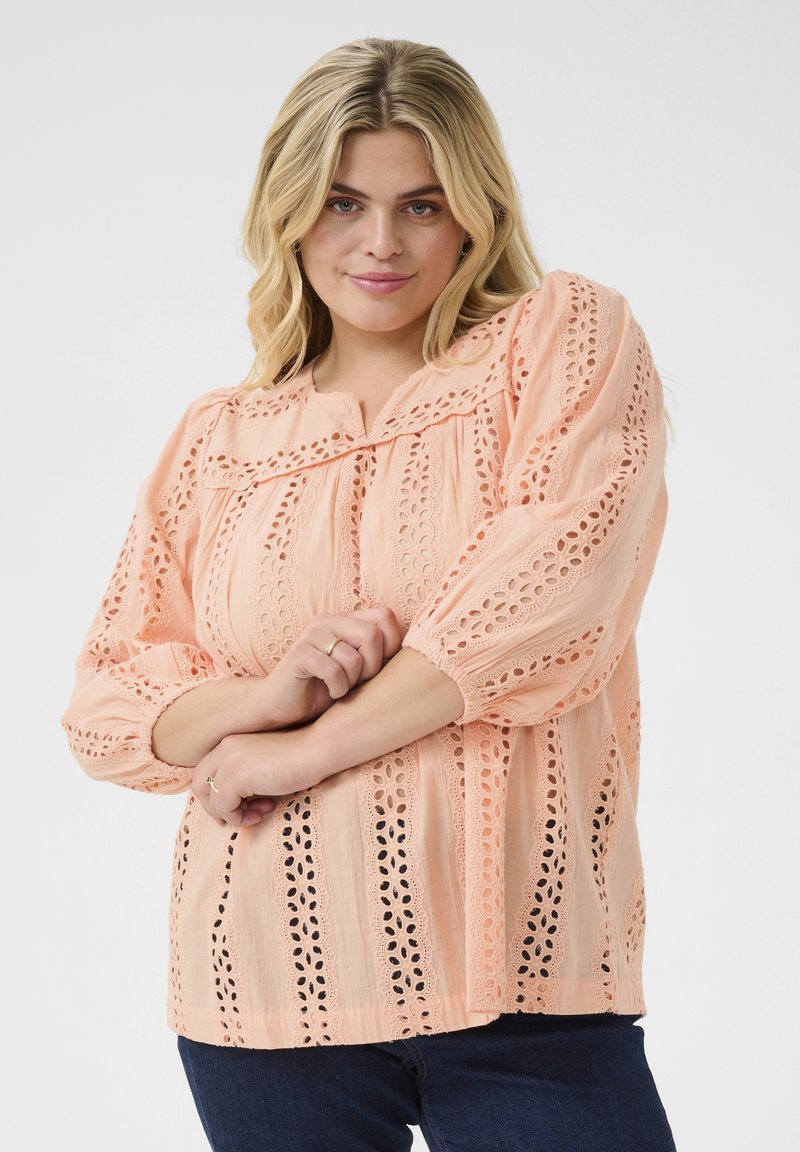 Light peach blouse with lace detailing, round neckline, and long, puffed sleeves. Features eyelet patterns and a relaxed fit.