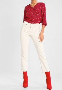 Blouse rouge à fleurs avec un col en V et des manches trois quarts, associée à un jean blanc court taille haute et des bottines rouges.