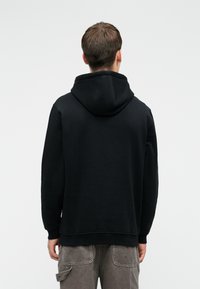 Μαύρη κουκούλα φτιαγμένη από βαμβακερό μείγμα, με ρυθμιζόμενη κουκούλα, ραμμένες μανσέτες και στρίφωμα, με καθαρό, μινιμαλιστικό σχέδιο.