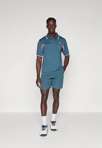 Rövid ujjú, türkizkék rövidnadrággal párosított rózsaszín kiemelésekkel, gallérral és gombos elülső résszel. Nedvességelvezető anyagból készült.