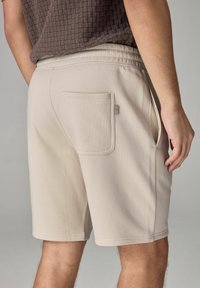 Short beige avec une texture lisse, doté de poches latérales et d'une poche arrière. La ceinture est élastiquée pour plus de confort.