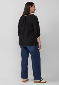 Zwarte textuurtop met driekwartmouwen, gecombineerd met blauwe straight-leg jeans en sneakers met een crèmekleurig en bruin ontwerp.