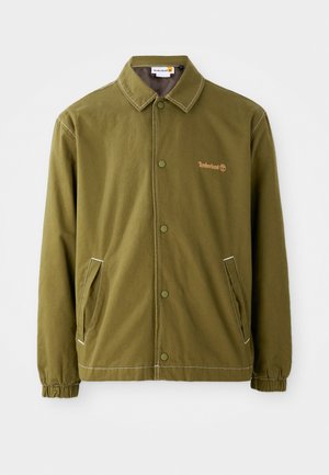 Olivgrüne Jacke aus strapazierfähigem Stoff, mit Kragen, Druckknöpfen, Seitentaschen und weißen Nähten. Timberland-Logo sichtbar.