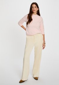 Helles rosa Strickpullover mit Rundhalsausschnitt, kombiniert mit cremefarbenen, weit geschnittenen Hosen. Der Look zeichnet sich durch subtile Texturen und eng anliegende Ärmel aus.