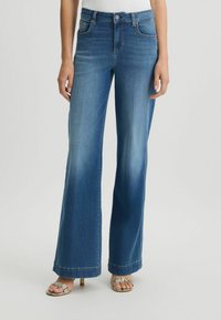 Pantalon en denim bleu à jambes larges avec une finition délavée. Les caractéristiques incluent cinq poches, une fermeture à bouton et un ourlet brut en bas.