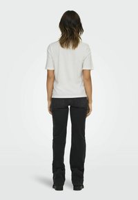 Hvid bomulds t-shirt med oprevet ærmer, parret med sorte jeans, der har lige snit og et enkelt design, set fra ryggen.