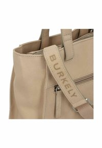 Bolso de mano de piel beige con cierre de cremallera, una correa texturizada con la marca "BURKELY" y un bolsillo lateral con cremallera y tira metálica.