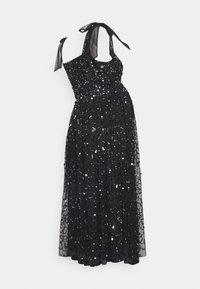 Robe maxi noire en sequins avec un corsage ajusté, une superposition transparente et des nouettes au cou. Elle présente une jupe fluide et des motifs complexes de sequins.