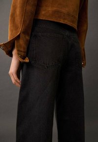 Mustat farkut suoralla lahkeella, joissa on takataskut ja korkea vyötärö. Yhdistetty ruskeaan mokkanahkasta valmistettuun lyhytjakkuun.