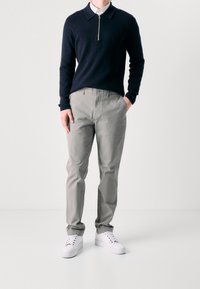 Navy zip-neck sweater, gray cotton pants, and white sneakers. The sweater has a collar, while the pants have a flat front and belt loops.