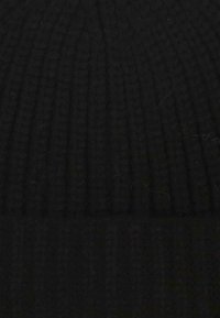 Berretto in maglia nera con una texture a coste. Il tessuto appare morbido e flessibile, progettato per adattarsi comodamente attorno alla testa.