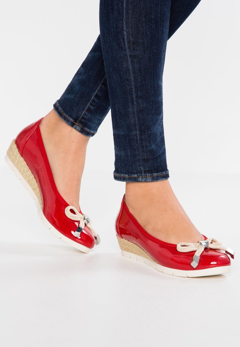 Chaussures compensées en cuir verni rouge avec un accent tressé beige et des éléments métalliques argentés, dotées d'un bout arrondi et d'une semelle texturée.
