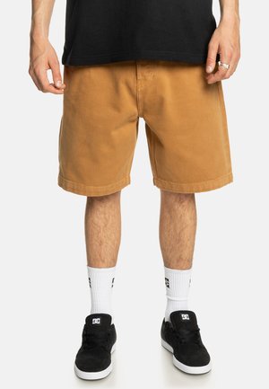 Tans kleurige katoenen shorts met een rechte snit, zijzakken en een omgeslagen onderrand. Gepaard met zwarte schoenen en witte sokken met een logo.