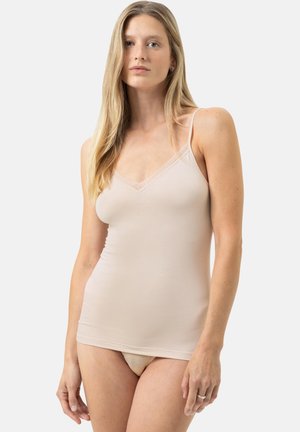 Woman with long blonde hair wearing a beige camisole top and matching underwear, standing against a plain light background.