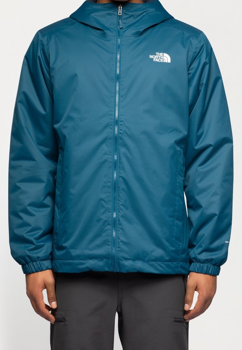 Veste imperméable turquoise avec une fermeture éclair à l'avant, capuche ajustable, poignets élastiques et logo sur la poitrine gauche. Matériau léger.