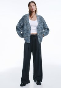 Gestrickter, übergroßer grau-blauer Cardigan mit lockerem Sitz, gerippter Struktur und fünf großen Knöpfen, kombiniert mit schwarzen Hosen mit weitem Bein.