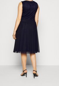 Marinblå klänning med spetsbyst, utsvängd tyllkjol och smal midja. Ett par svarta klacksandaler fulländar outfitten.