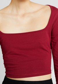 Burgundin pitkähihaine crop-top pehmeästä, muotoon puristavasta puuvillasta, jossa on leveä neliön muotoinen kaula-aukko ja saumaton helma, joka korostaa vyötä.