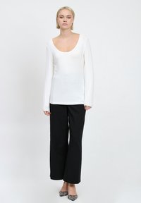Weißes Langarmoberteil mit Rundhalsausschnitt, kombiniert mit schwarzen weiten Hosen. Das Outfit zeichnet sich durch minimalistisches Design und klare Linien aus.