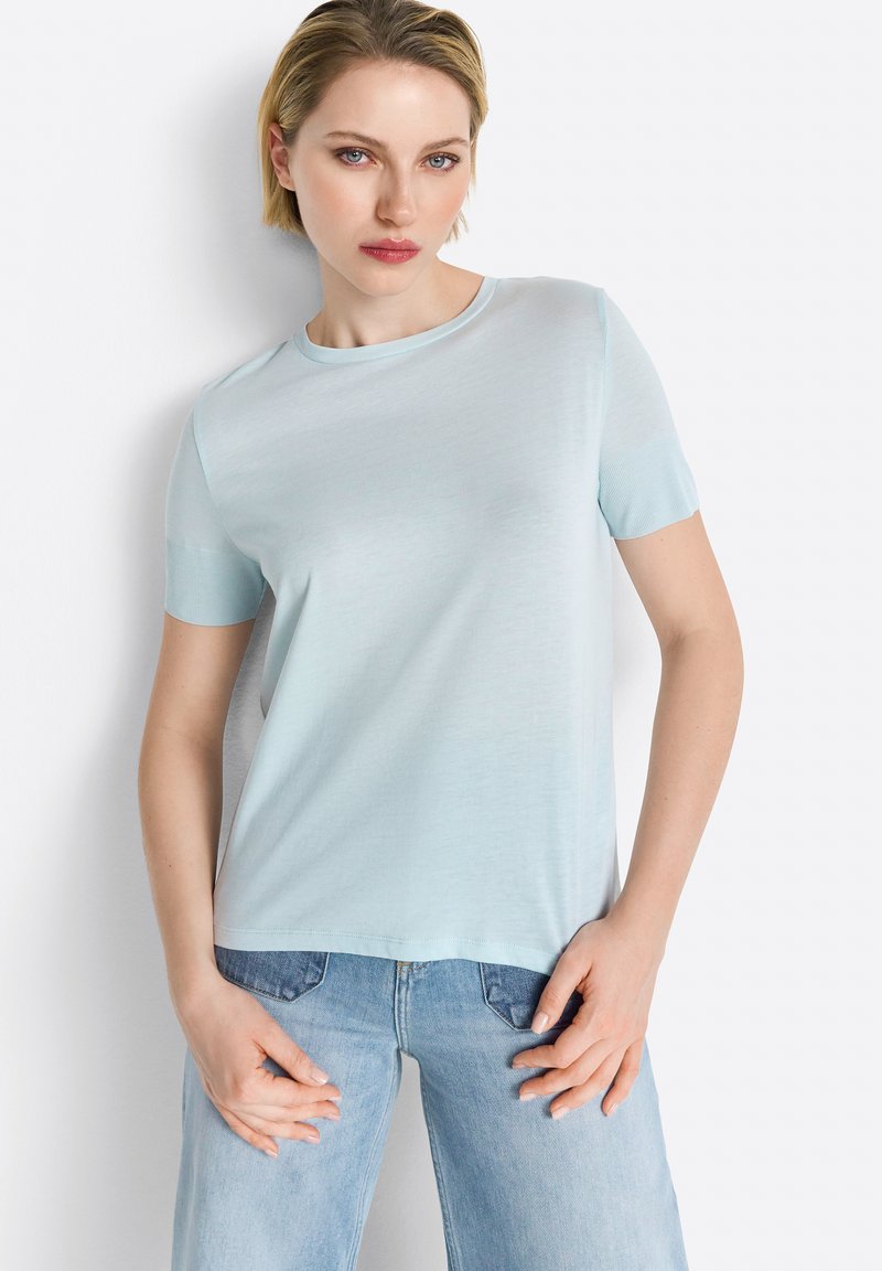 Tricou scurt cu mânecă scurtă de culoare albastru deschis, confecționat dintr-un material moale, având un guler rotund și o croială lejeră. Purtați-l cu blugi de culoare albastru deschis.