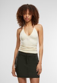 Lys gul halterneck-top med V-hals og pynt, parret med en sort nederdel med lommer og en struktureret design.