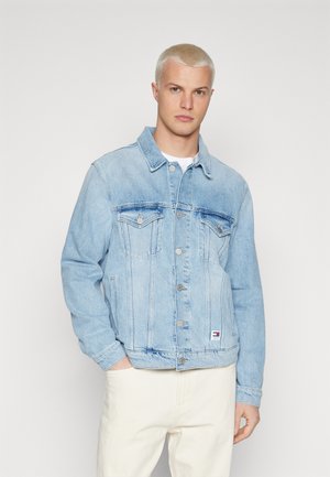 Chaqueta de mezclilla azul claro con un diseño clásico, cierre de botón, dos bolsillos en el pecho y una pequeña etiqueta en el dobladillo. Textura desgastada en toda la prenda.