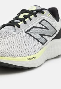 Zapatilla deportiva gris con parte superior de malla, acentos en negro y suela de espuma amarilla etiquetada como "FRESHFOAM". Presenta cordones negros y un patrón texturizado.