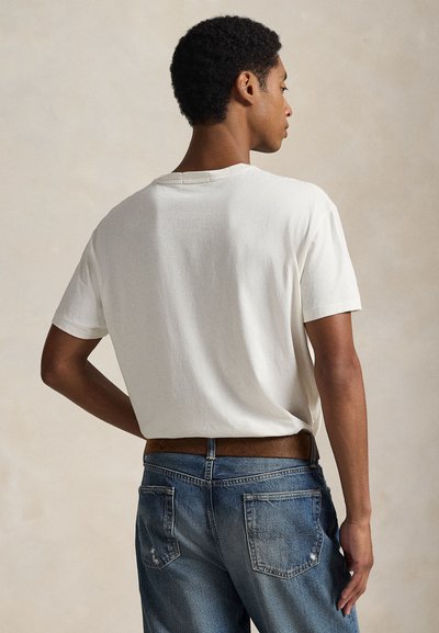 Fehér pamut póló rövid ujjakkal, laza szabással és kerek nyakkivágással, kék farmernadrággal, amely enyhén kopott mintázattal rendelkezik.