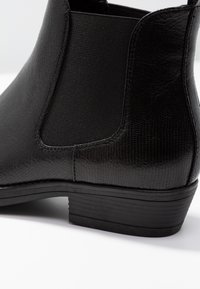Bottes chelsea noires en cuir texturé avec des panneaux latéraux élastiques, un petit talon empilé et une semelle en caoutchouc lisse.