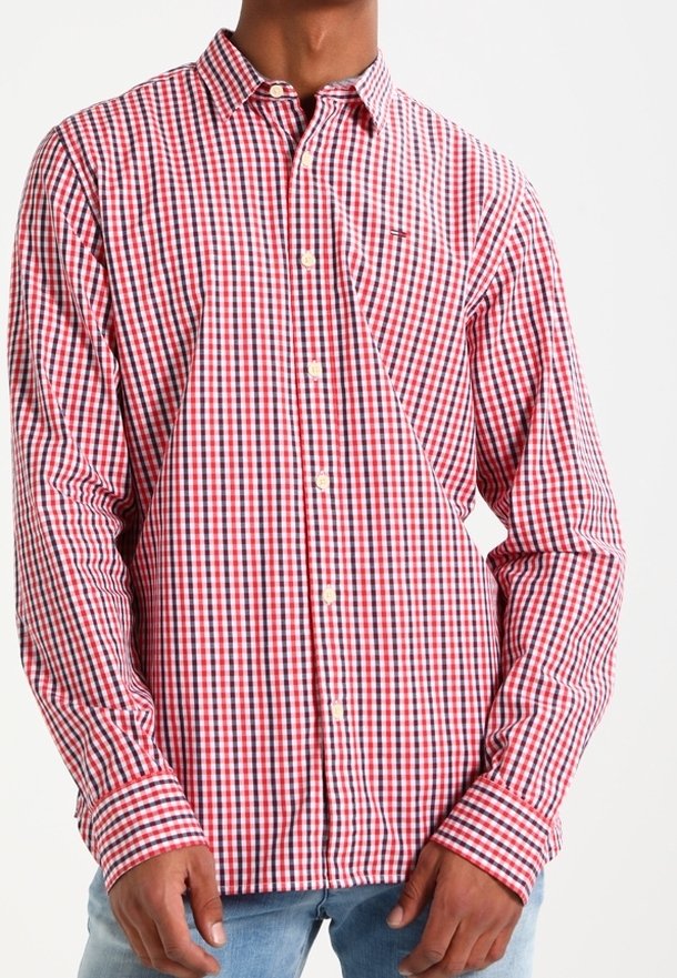 Camisa de manga larga a cuadros rojos y blancos, con cuello abotonado, que presenta un logo en el pecho y botones a lo largo del frente, combinada con denim azul claro.