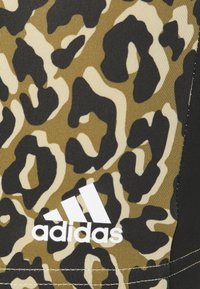 Adidas activewear med et brun og sort leopardprint-design, tekstureret stof, med en kontrasterende hvid logo nederst til venstre.