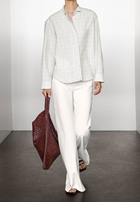 Chemise boutonnée blanche à carreaux, pantalon blanc ample et sac fourre-tout tissé bordeaux. Tissu lisse et coupe décontractée avec des manches longues et un col ouvert.