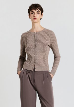 Light brown knitted cardigan with a ribbed texture, round neckline, and button closure. Paired with pleated, tapered brown trousers.