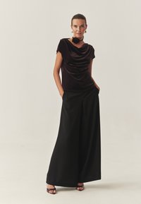 Vellustop i dyb lilla, kombineret med vide sorte bukser. Har en blomster-accent halskæde og minimalistisk design.