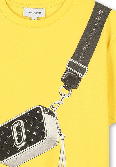 T-shirt jaune avec un graphique d'un sac à main noir et blanc orné de fleurs, de matériel argenté et d'un détail de bandoulière contrastant.