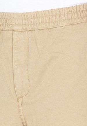 Beige lightweight pants featuring an elastic waistband, side pocket, and smooth, textured fabric. Suitable for casual wear.