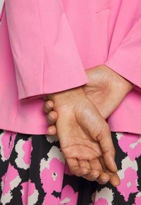 Pink blazer med en struktureret silhuet og glat tekstur, parret med en sort nederdel med et dristigt pink og hvidt abstrakt mønster.