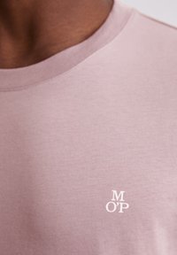 Jasnoróżowa bawełniana koszulka z okrągłym dekoltem i małym białym nadrukowanym logo "M O'P" na lewej klatce piersiowej. Miękka w dotyku, minimalistyczny design.