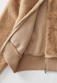 Giacca zip-up beige con un esterno morbido e soffice, polsini e orlo a costine, e una fodera interna liscia di una tonalità più chiara.