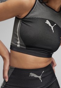 Sort ærmeløs sports crop top med et struktureret mønster, der har et Puma-logo i hvid og kontrasterende striber i et stribet design.
