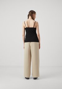 Black camisole with thin straps paired with high-waisted, wide-legged beige trousers. Smooth fabric texture with a neutral color palette.