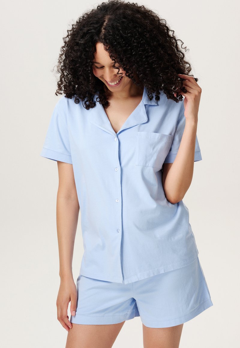Lichtblauwe katoenen pyjama set bestaande uit een kortgerafelde button-up top met een borstzak en bijpassende shorts, zachte textuur, casual ontwerp.
