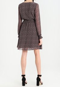 Vestido de manga larga con un estampado floral oscuro, cintura ajustada y una silueta fluida. Combinado con tacones negros con tira en el tobillo.